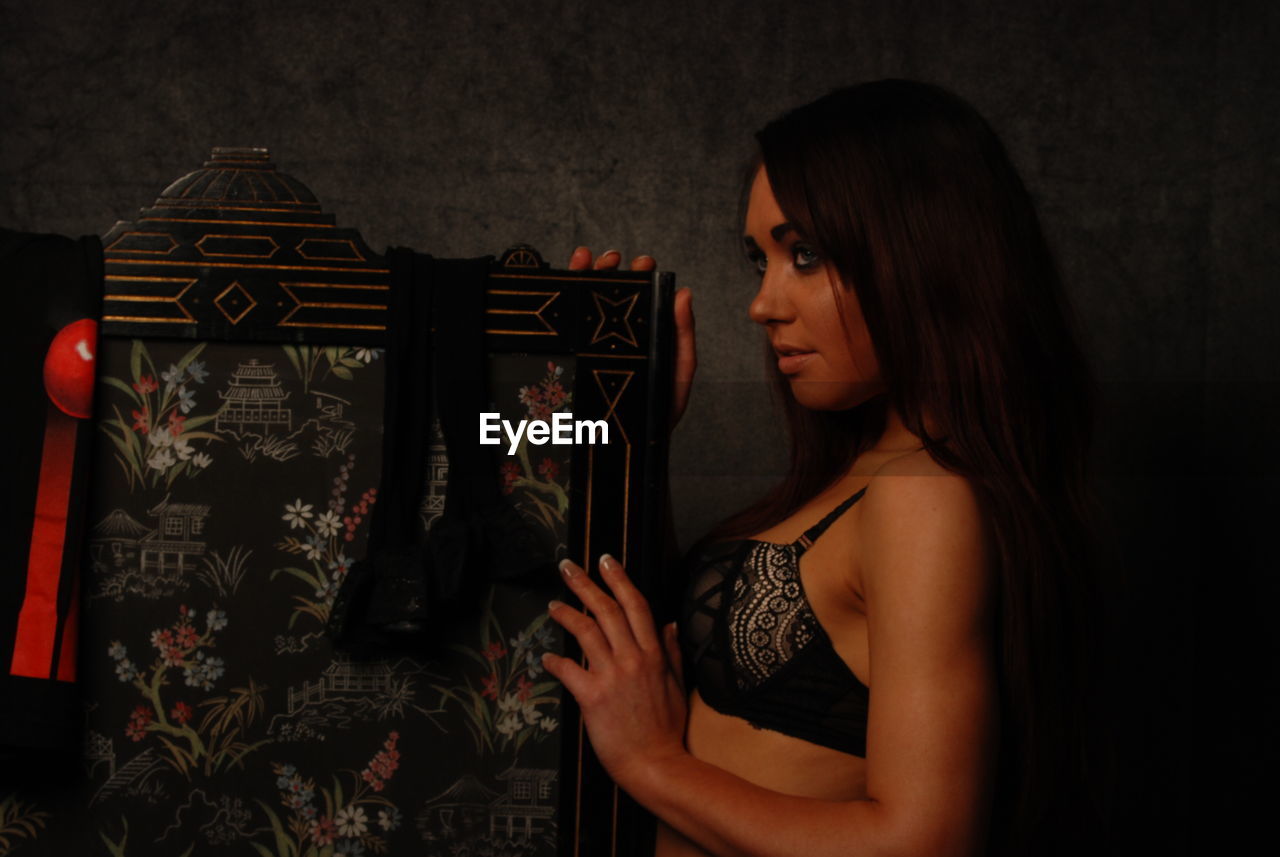 SIDE VIEW OF YOUNG WOMAN LOOKING DOWN WHILE STANDING IN CORRIDOR