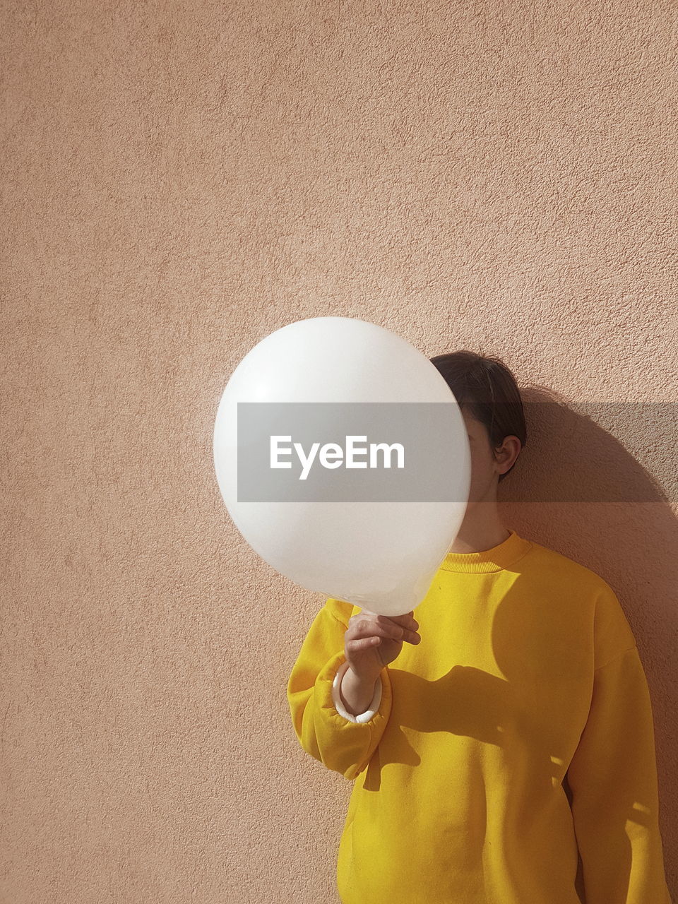 Woman covering face with balloon against wall