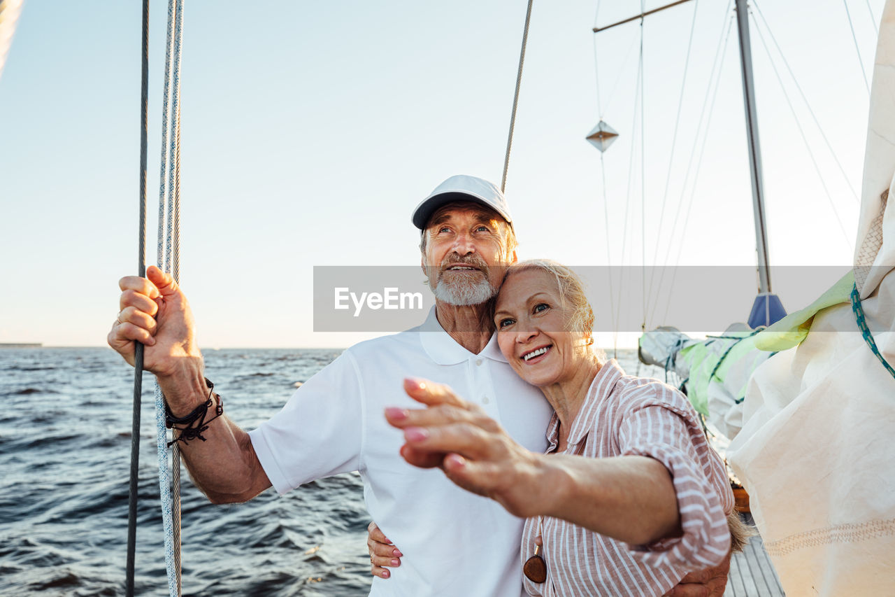 Smiling senior couple on sailboat in sea against sky