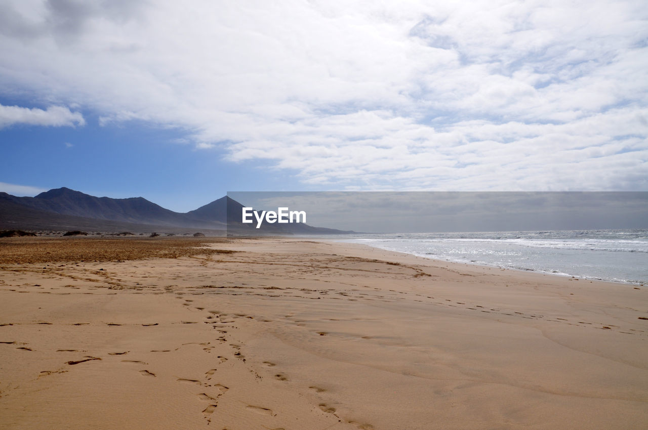 Scenic view of sandy beach against cloudy sky