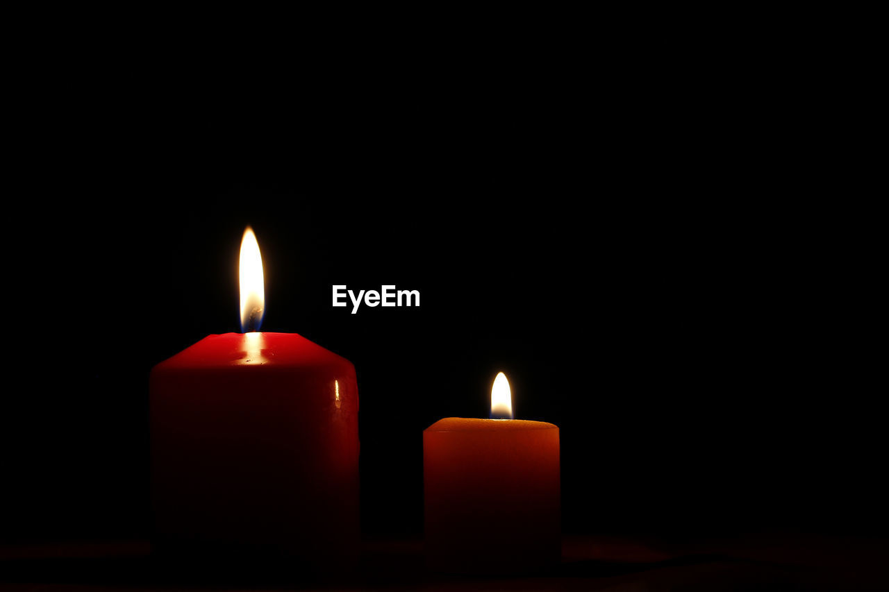 Close-up of burning candles against black background