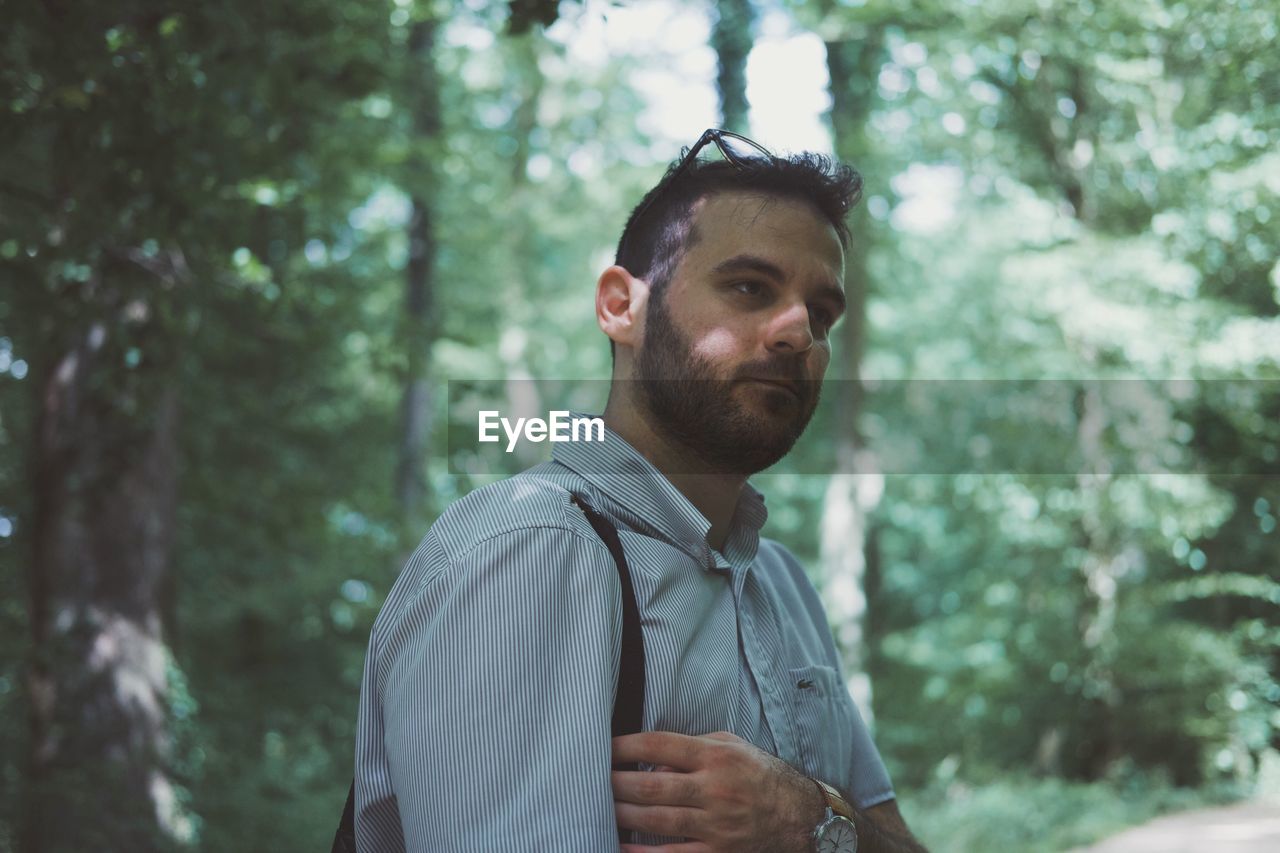 Young man looking away while standing in forest