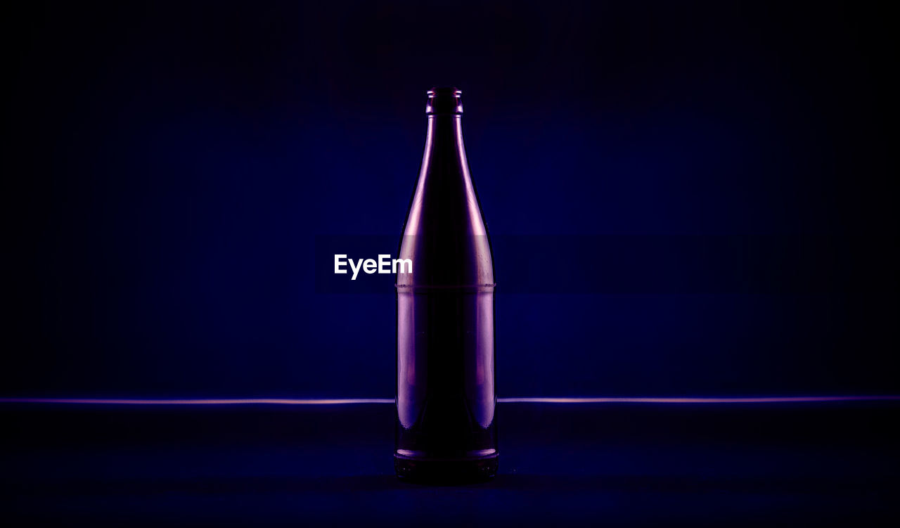 Close-up of illuminated beer bottle on table against black background
