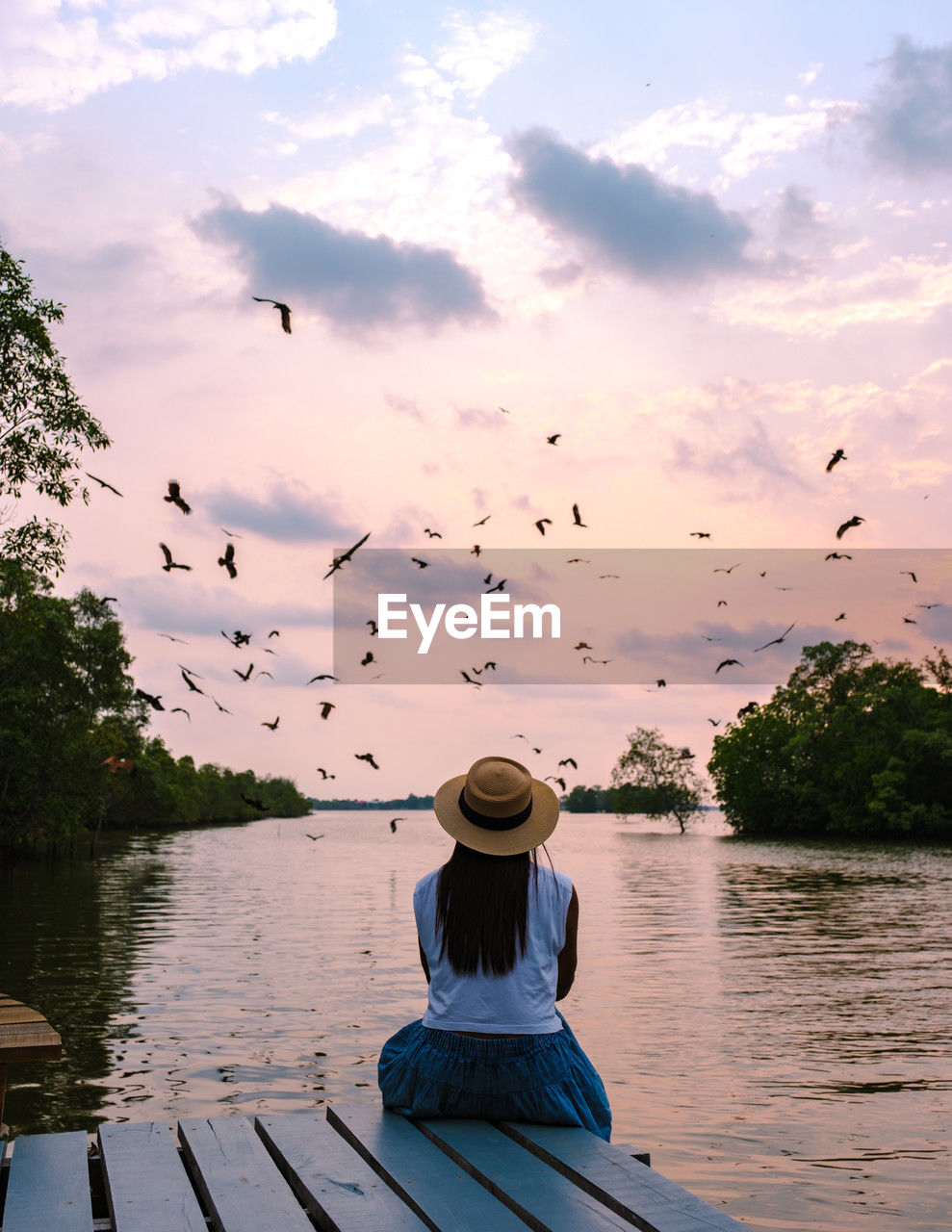 rear view of woman sitting on pier over lake against sky during sunset