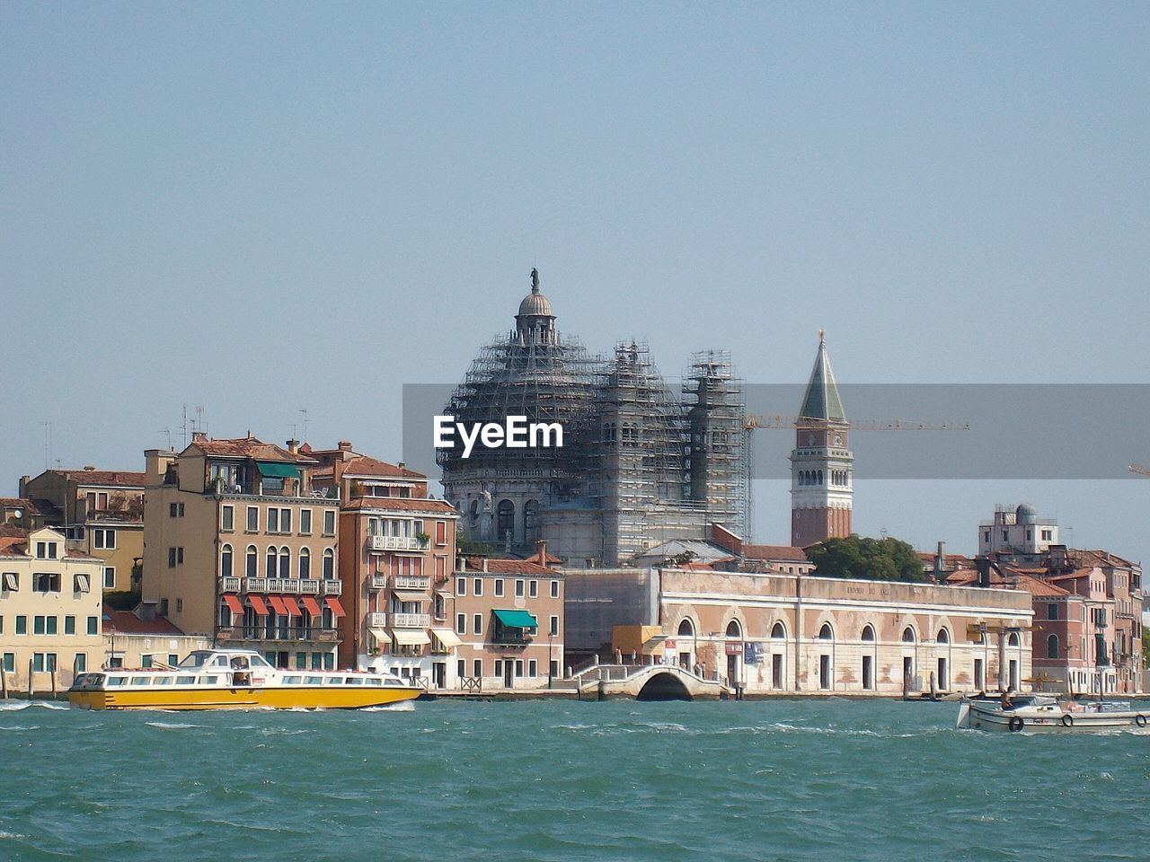 San marco campanile and incomplete santa maria della salute by canal against clear sky