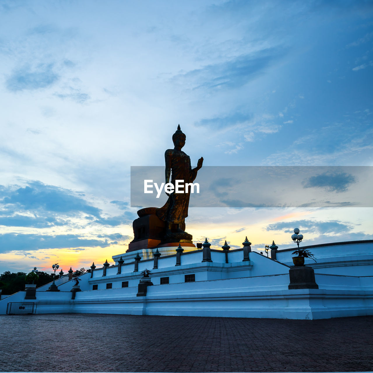 Statue by road against cloudy sky during sunset