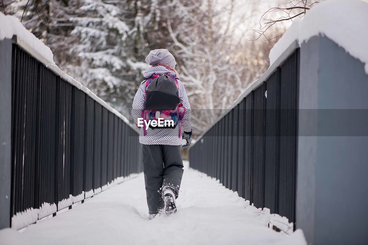 REAR VIEW OF WOMAN STANDING ON SNOW COVERED FIELD