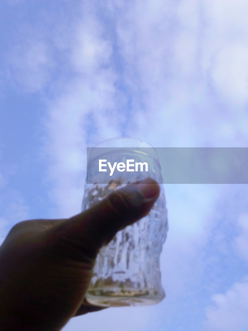 CROPPED IMAGE OF HAND HOLDING GLASS AGAINST SKY