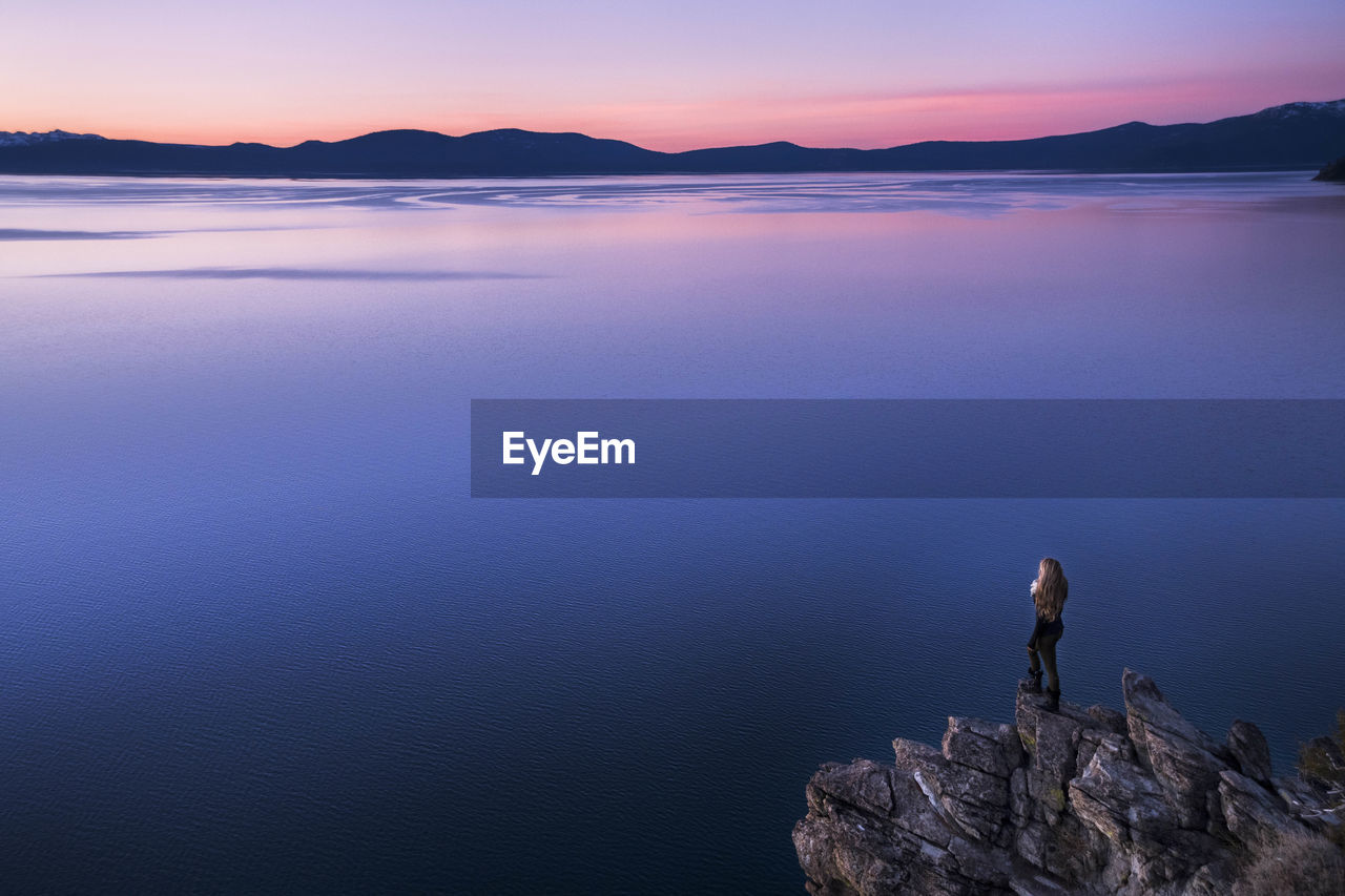 Woman looking at view while standing on rock formation by lake tahoe during sunset