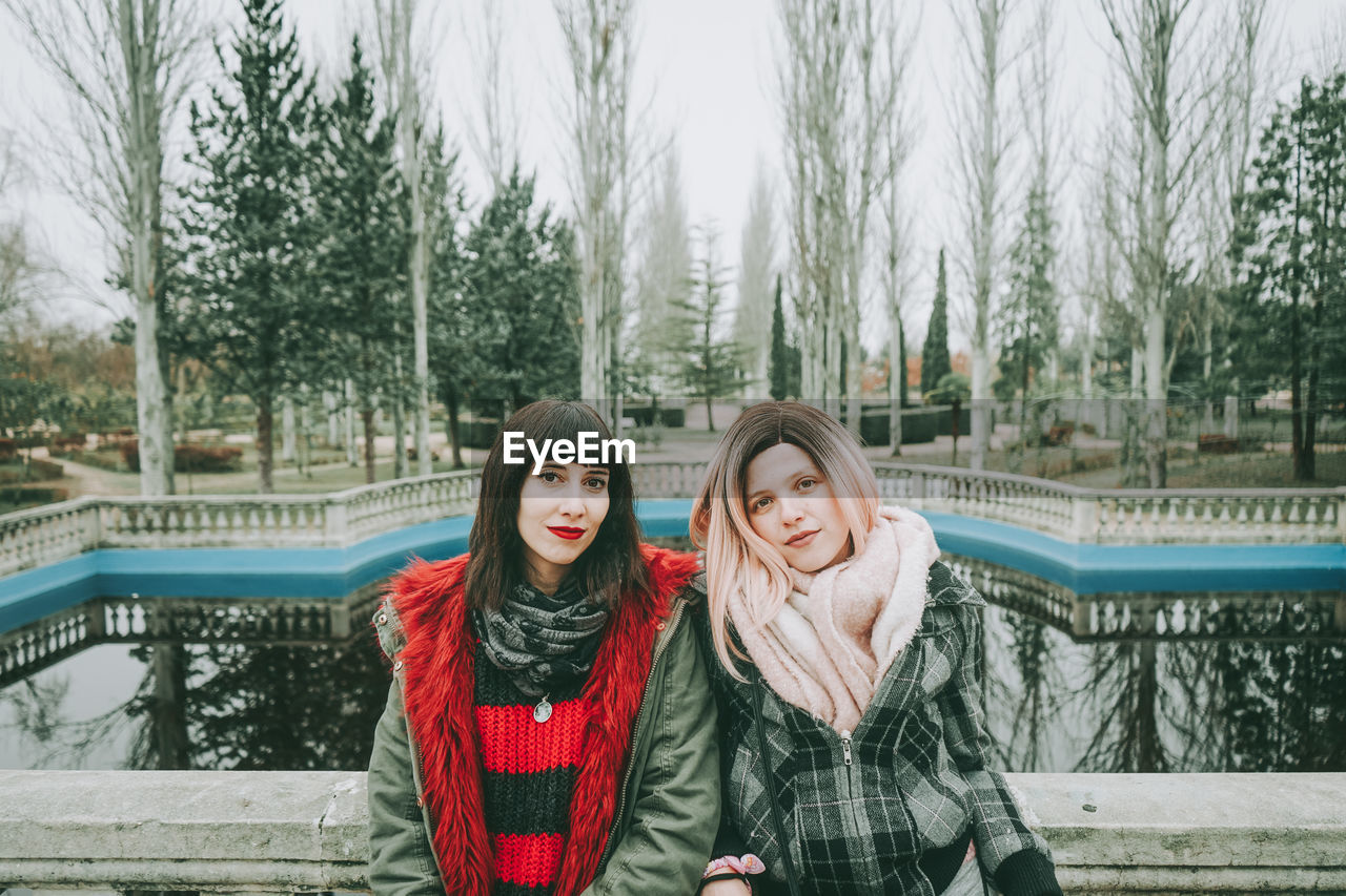 Portrait of smiling friends leaning on railing against lake during winter