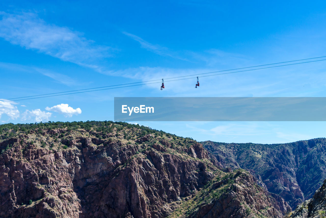 Low angle view of people on ski lifts over mountain against sky