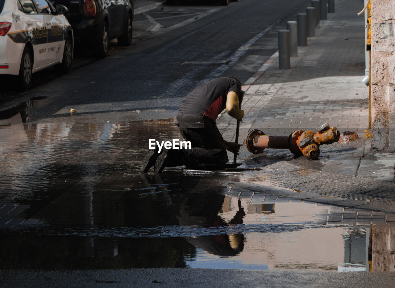 Man repairing fire hydrant on sidewalk in city