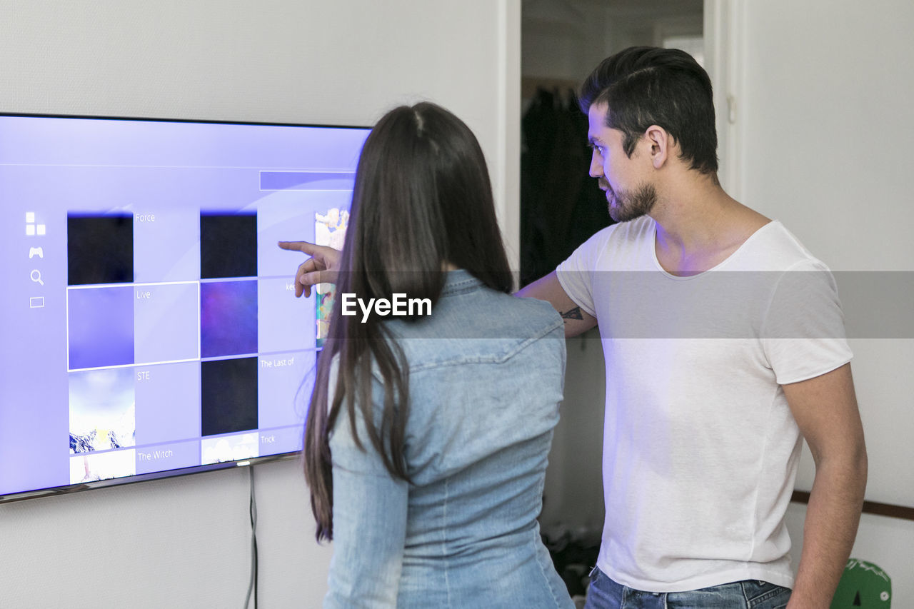 Young couple using touch screen television mounted on wall in living room