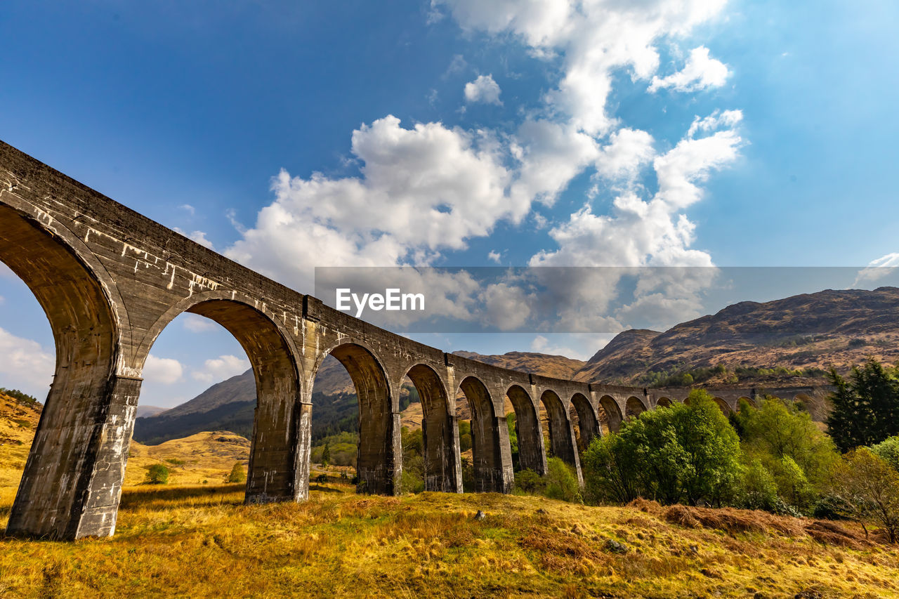 LOW ANGLE VIEW OF ARCH BRIDGE ON MOUNTAINS AGAINST SKY