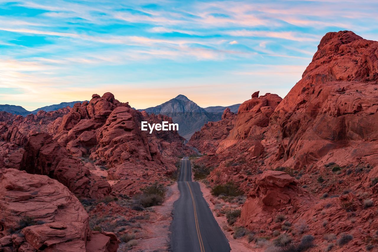 Empty country road amidst rock formations in desert against sky during sunset