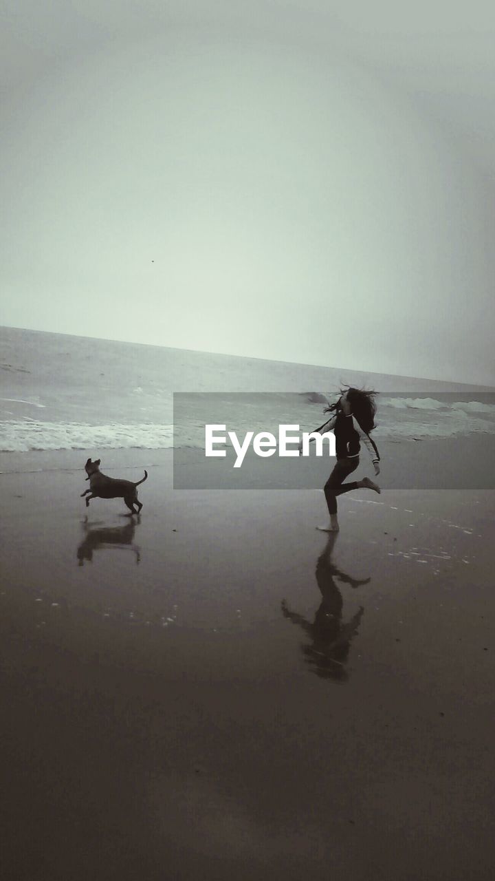 Girl running behind dog at beach