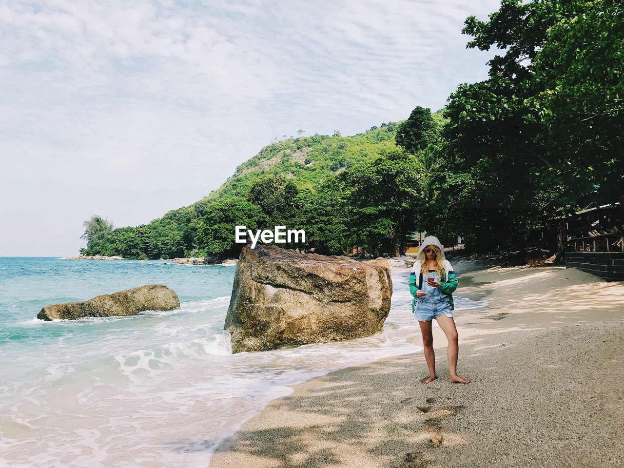 Full length of mid adult woman using mobile phone while standing at beach against sky