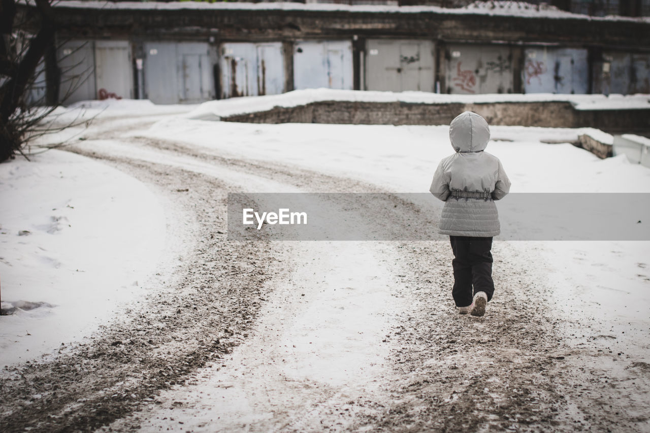 REAR VIEW OF MAN WALKING ON SNOW COVERED ROAD