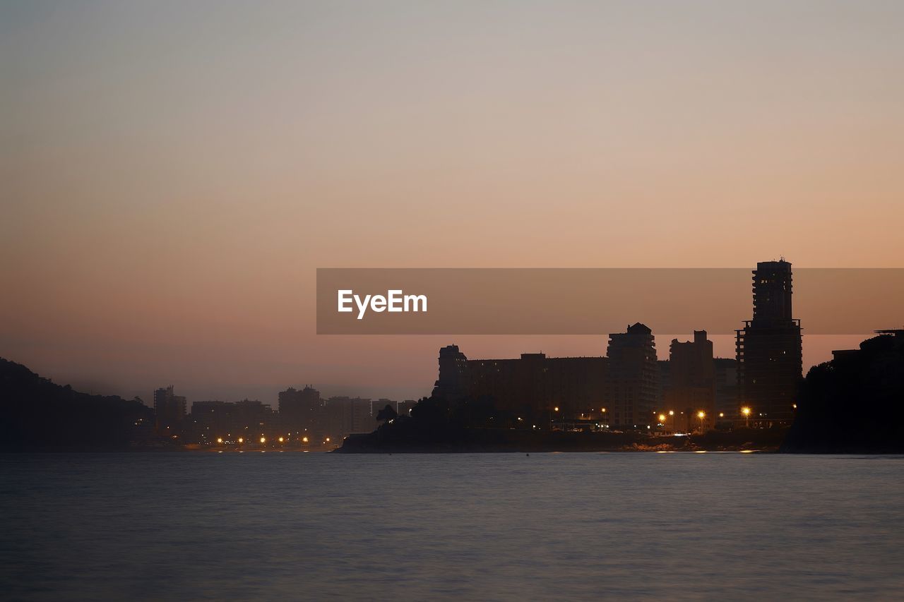 Silhouette buildings in city at sunset