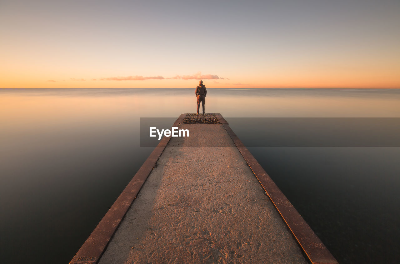 Man standing on jetty against sky during sunset