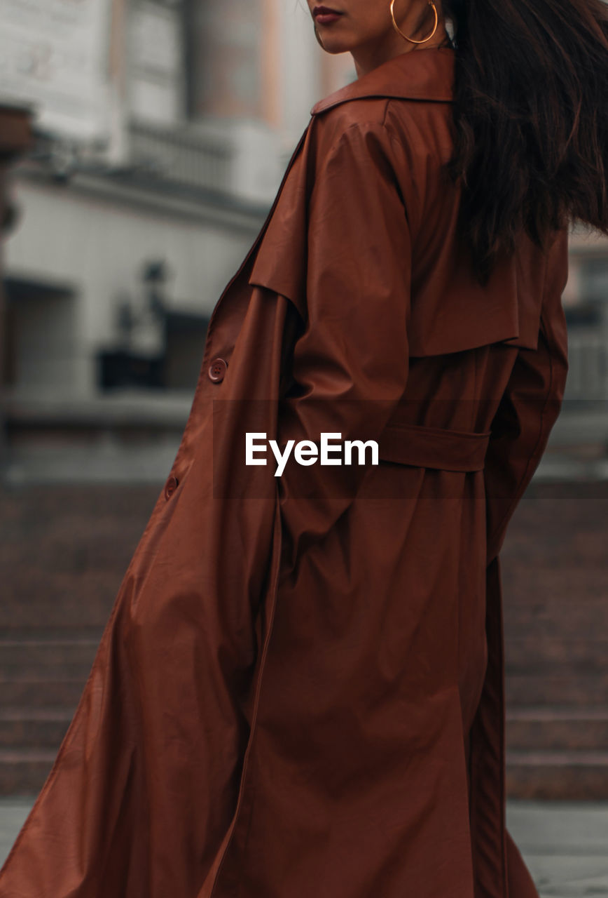 Fashion details of autumn brown leather trench coat. woman walking in the city. street style