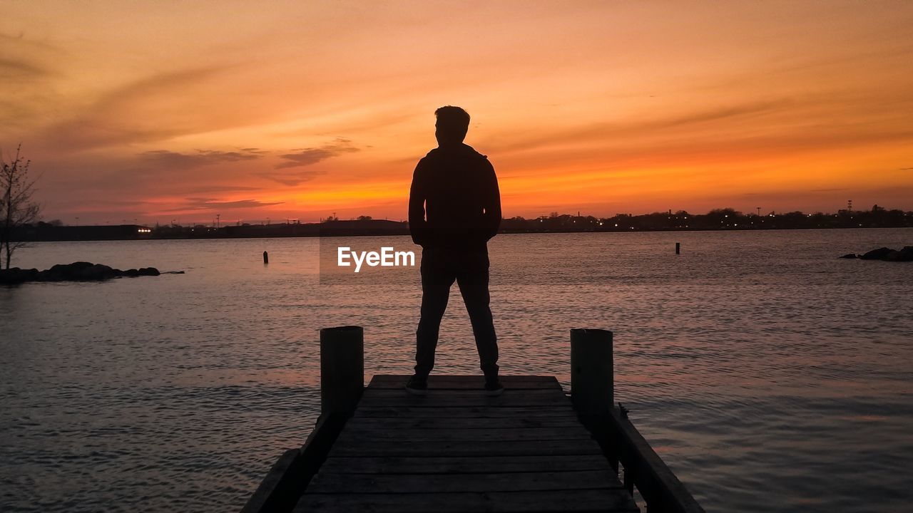 Silhouette man standing on pier over sea against sky during sunset
