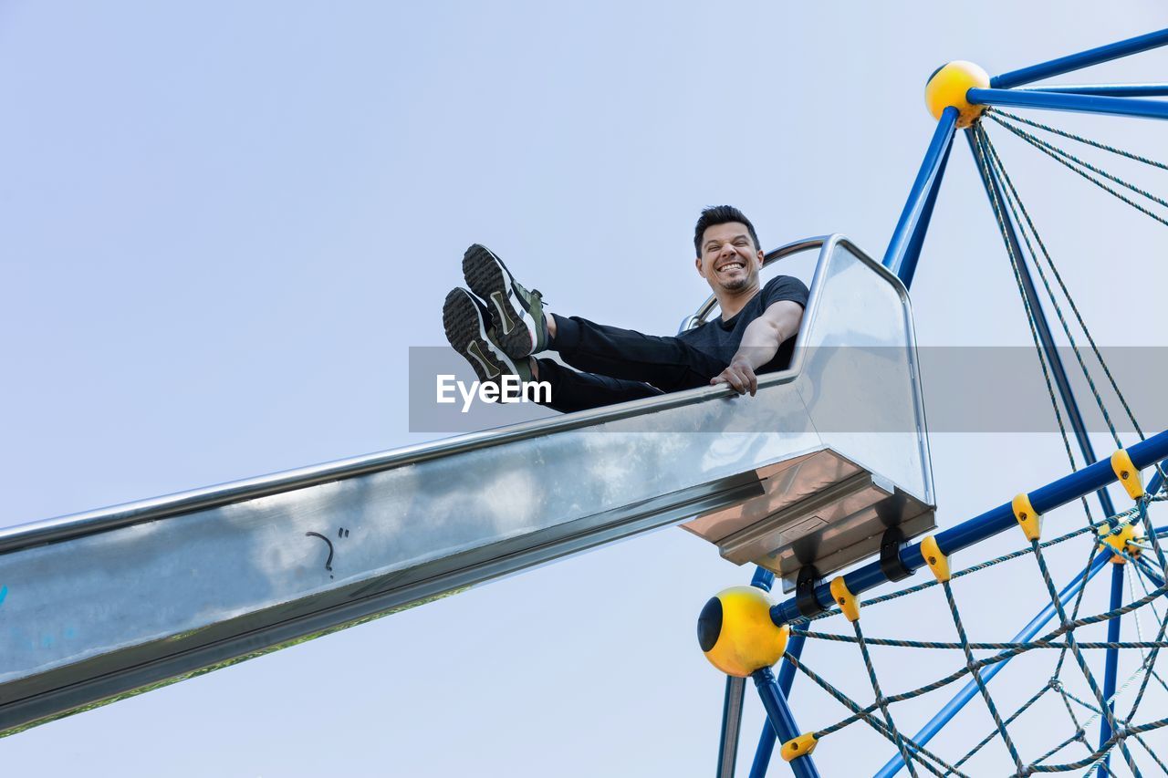 Low angle view of man sitting on slide against blue sky