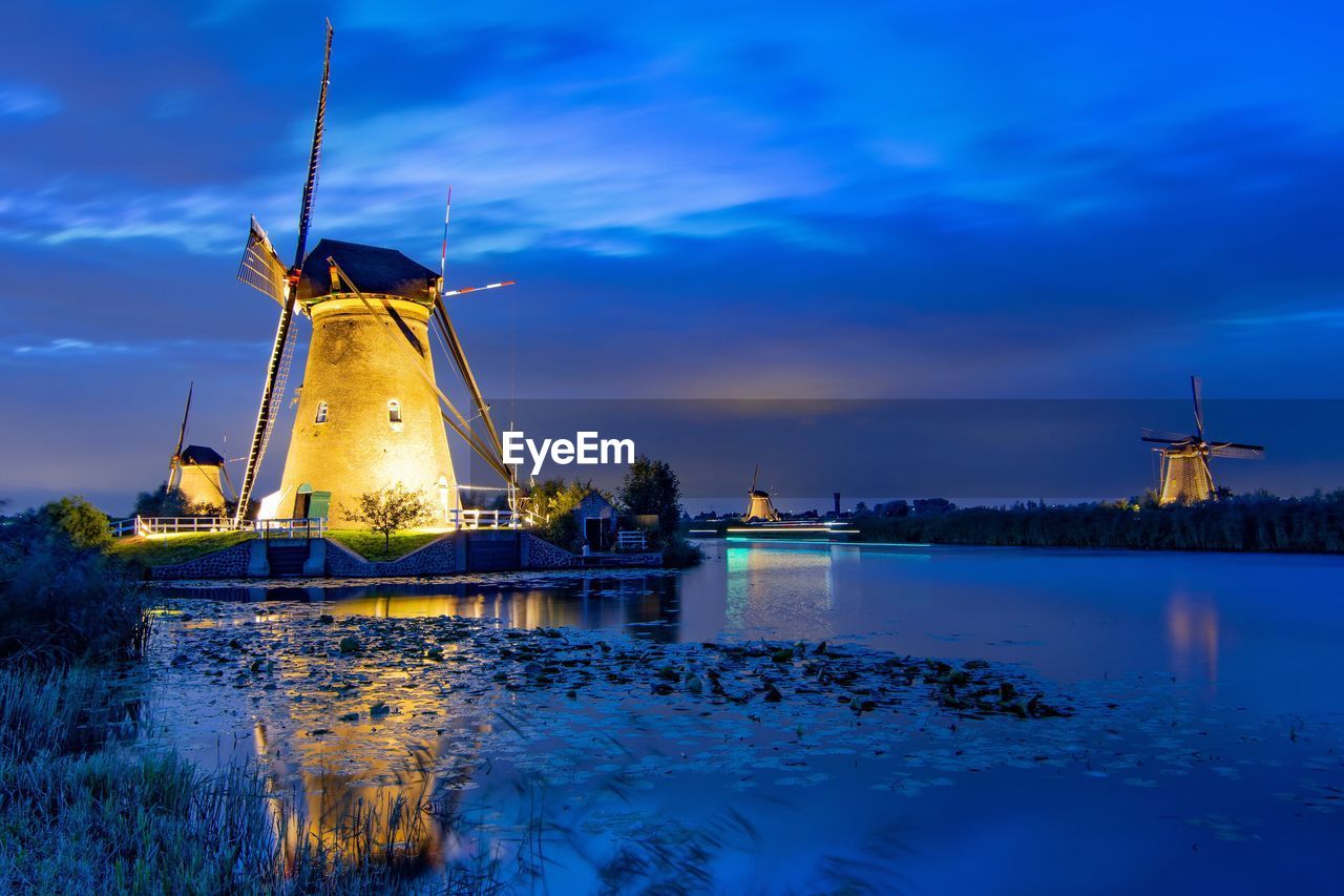 Traditional windmill by river against blue sky