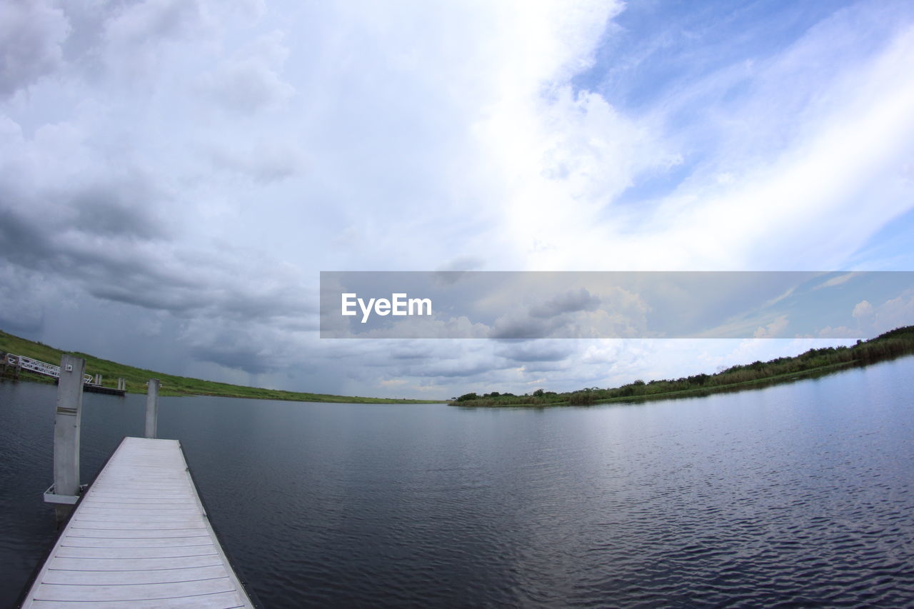 Fish-eye view of jetty in river against cloudy sky