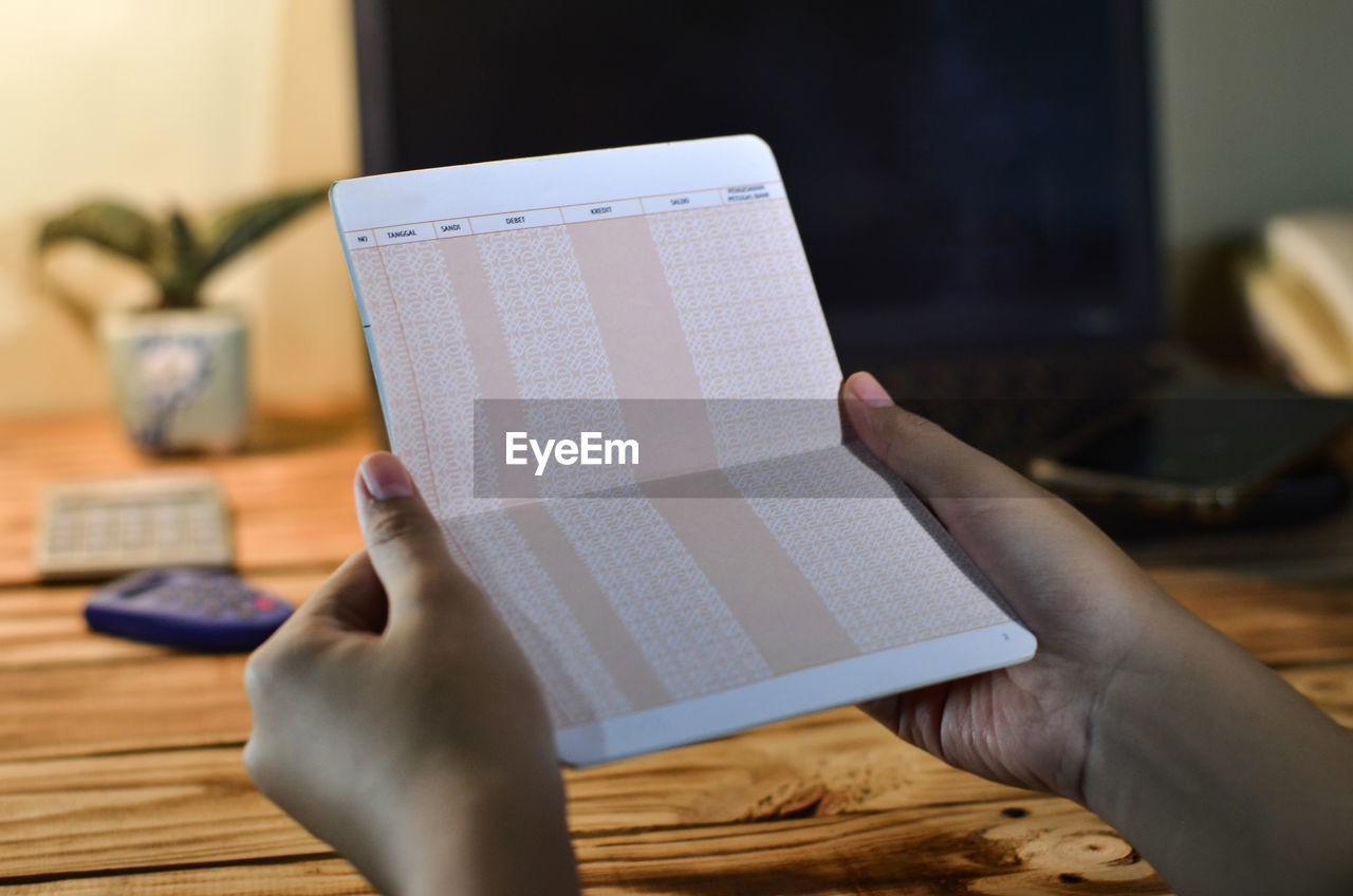 Hands holding passbook, on table with laptop background