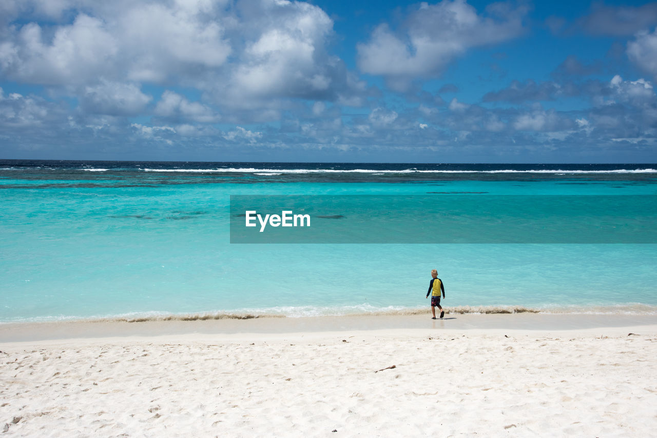 Rear view of boy walking at beach against sky