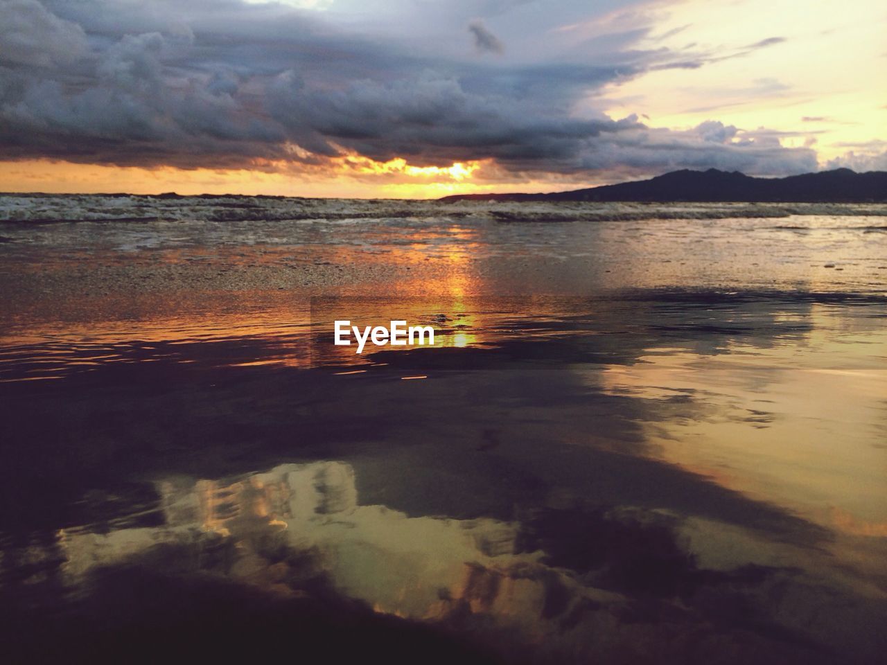 Scenic view of sea and silhouette mountains against cloudy sky