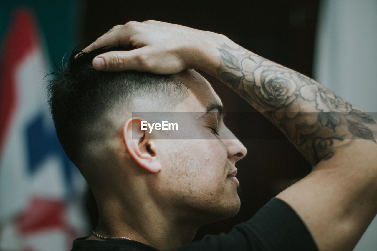 Close-up of young man with hand in hair while siting at barber shop