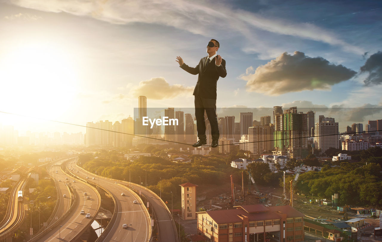 Full length of businessman with blindfold standing on rope in city during sunset