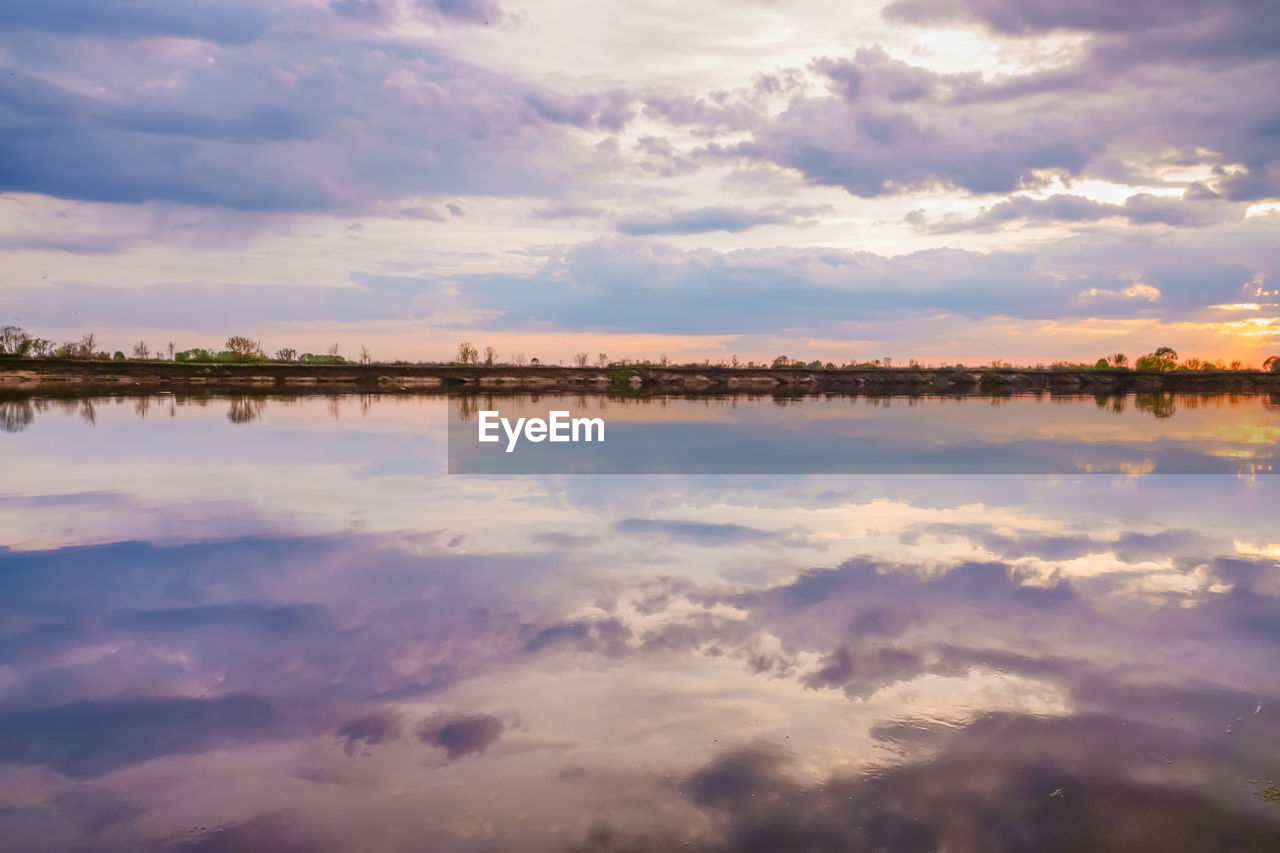 SCENIC VIEW OF LAKE AGAINST CLOUDY SKY DURING SUNSET