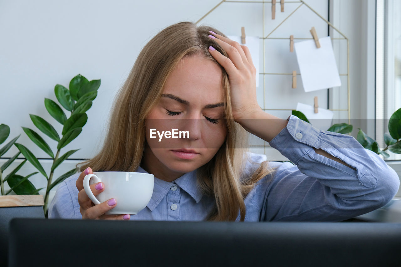 Tired sleepy young caucasian woman worker at desk workplace. overworking and sleeping deprivation. 