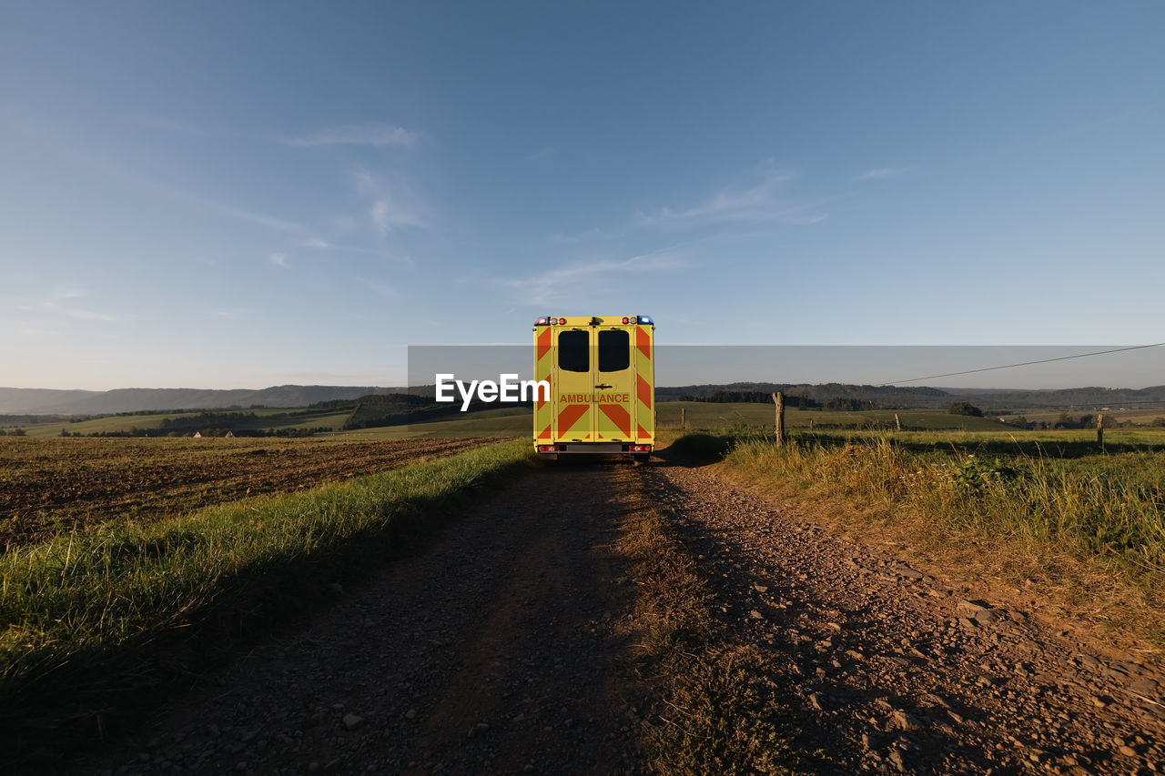 Ambulance car of emergency medical service leaving on rural dirt road in the middle of fields. 