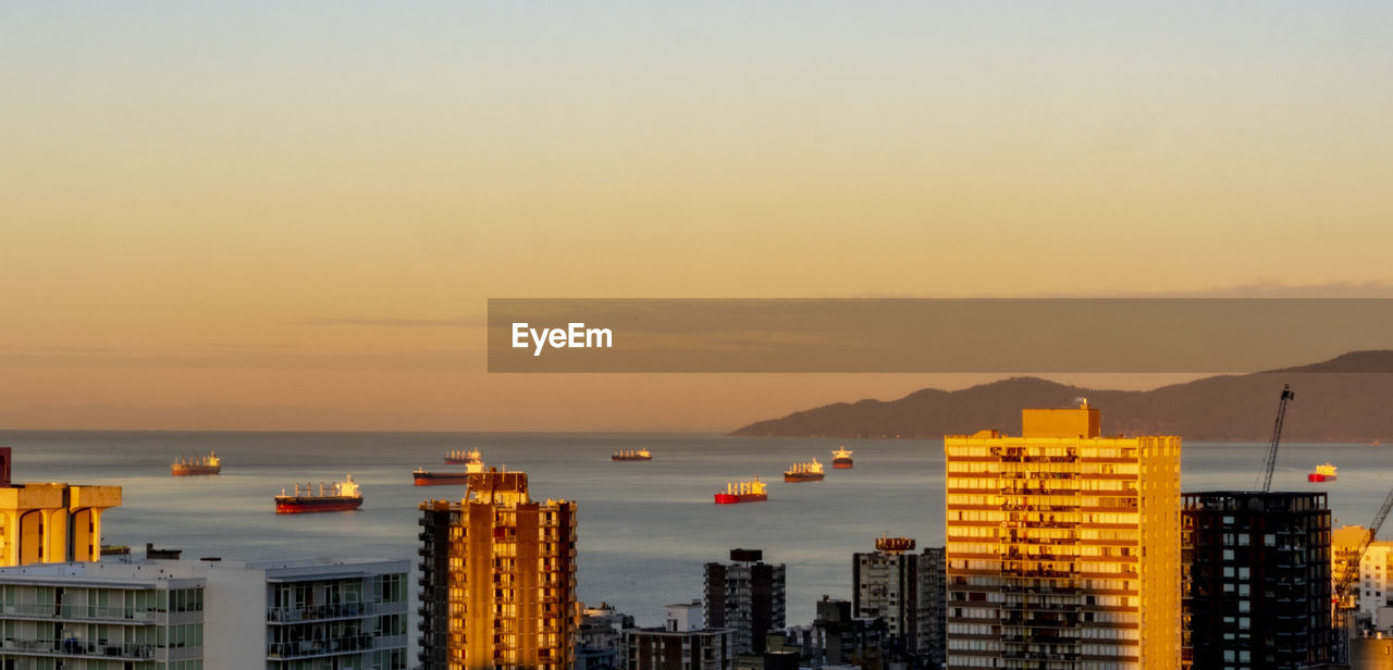 Sea by buildings against sky during sunset