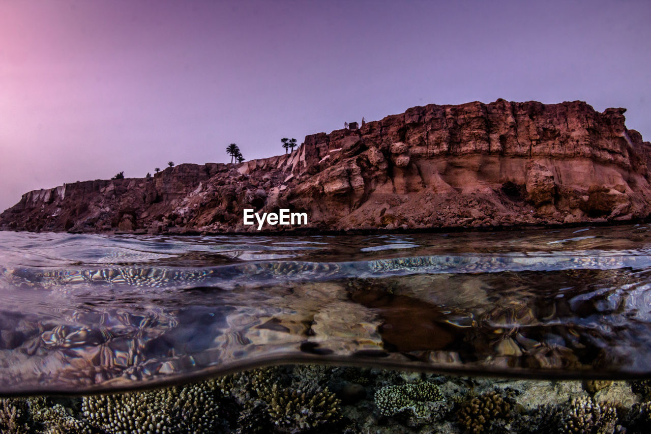 Scenic view of sea and rock formation against clear sky during sunset
