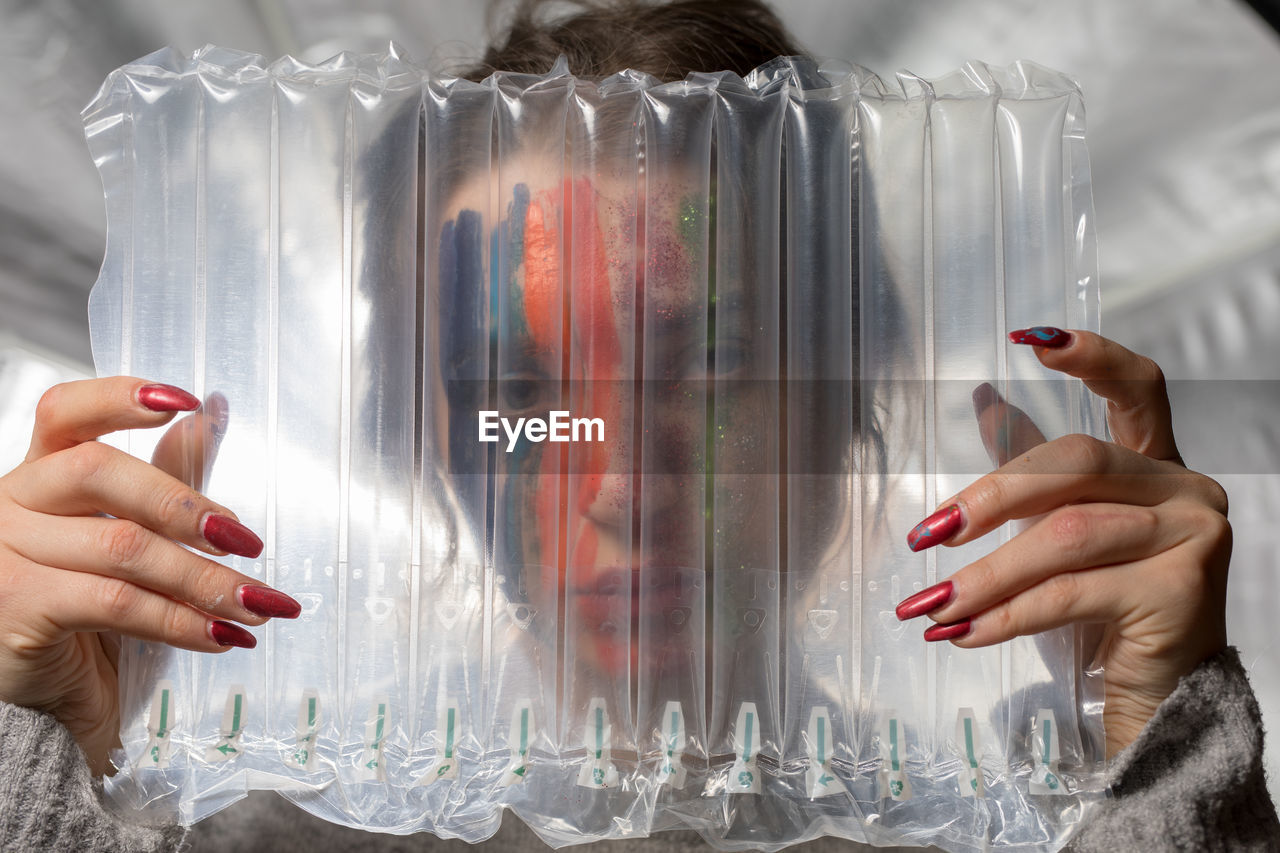 Close-up portrait of woman with painted face seen through plastic
