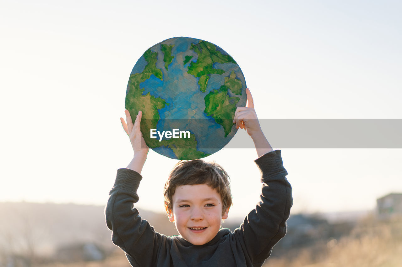 Portrait of cute boy holding globe against sky