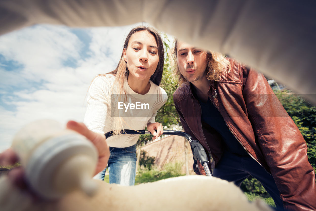 Portrait of smiling couple looking at baby stroller in park