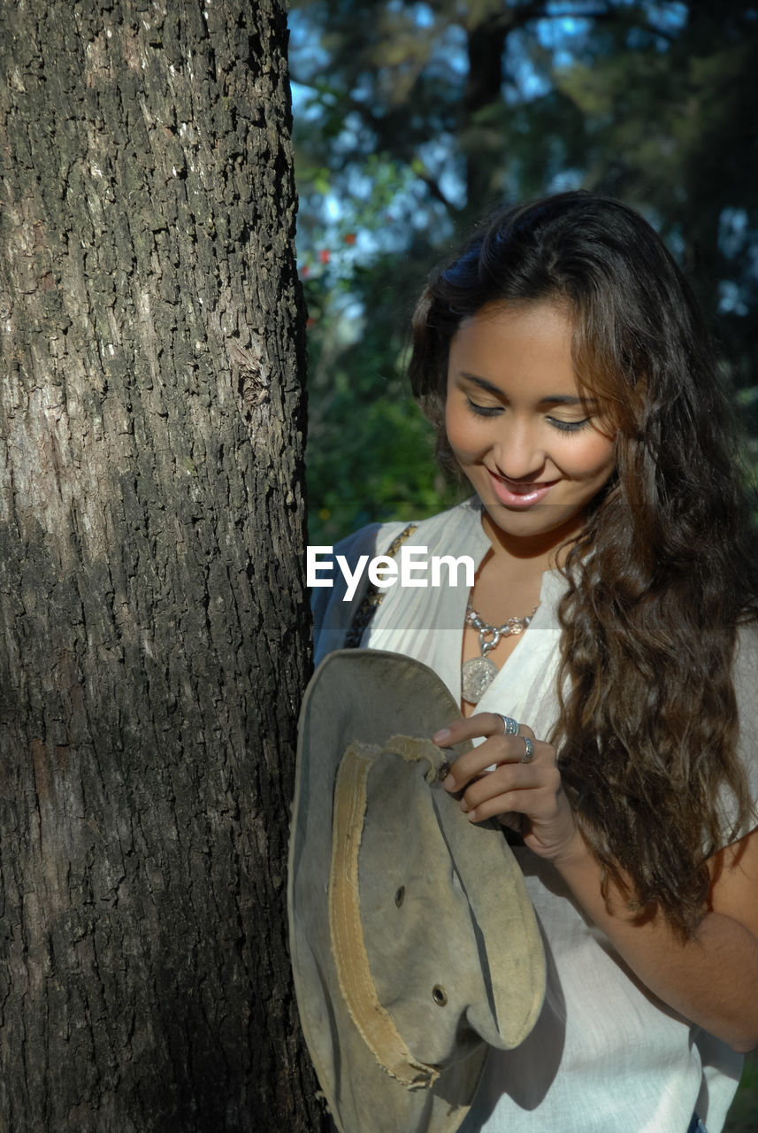 YOUNG WOMAN SMILING WHILE TREE TRUNK