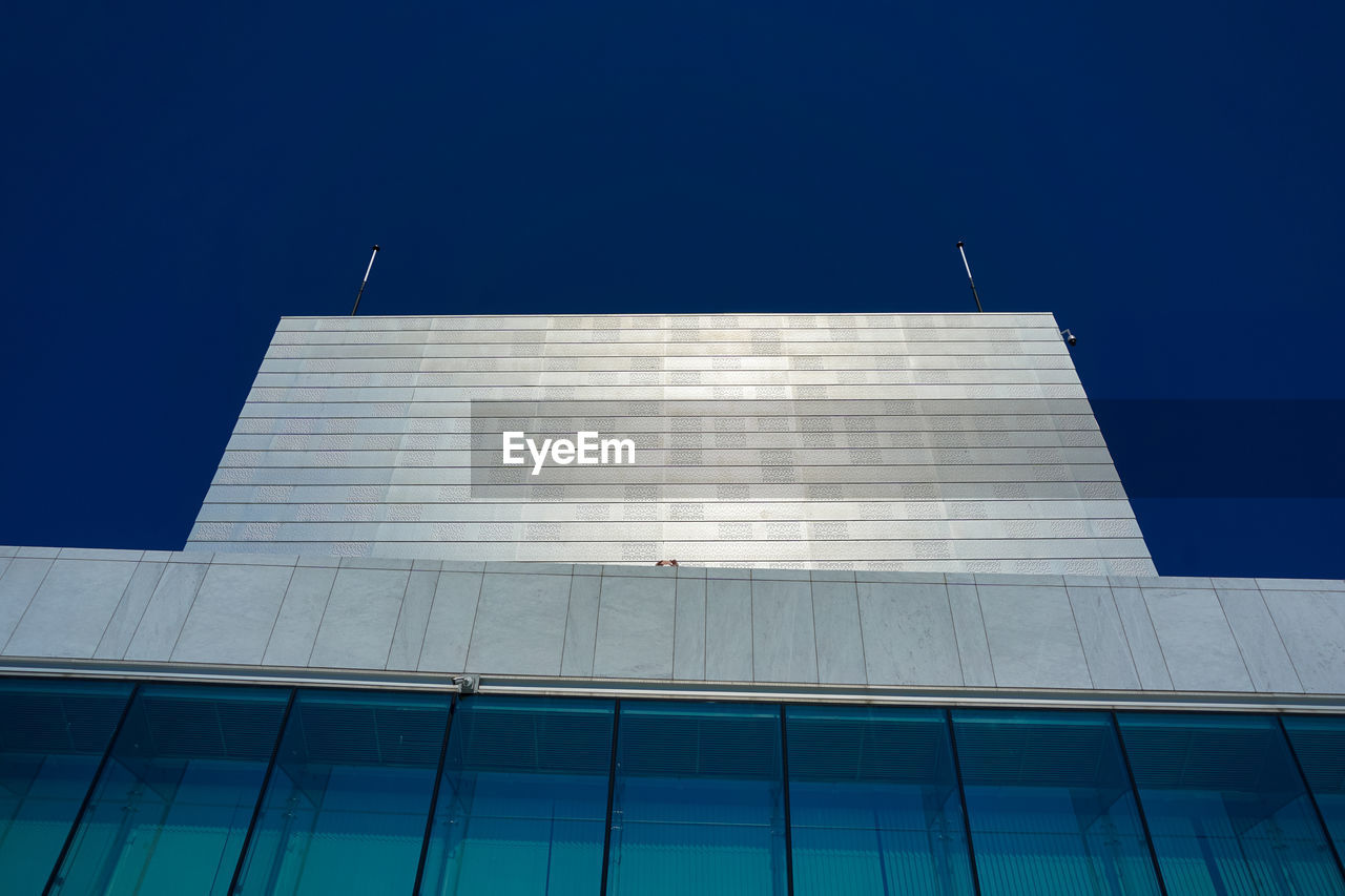 LOW ANGLE VIEW OF MODERN GLASS BUILDING AGAINST CLEAR BLUE SKY