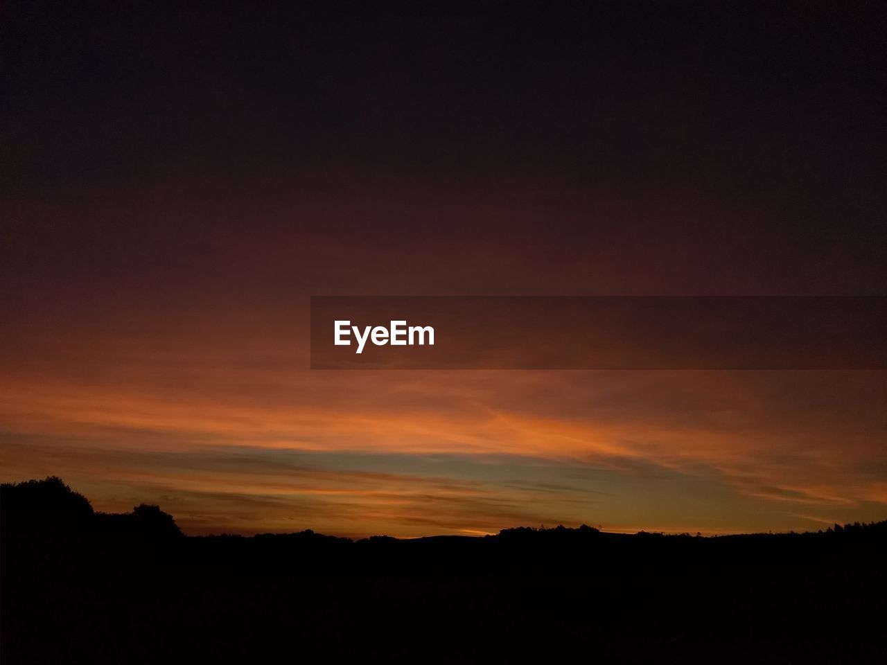 Silhouette landscape against dramatic sky during sunset