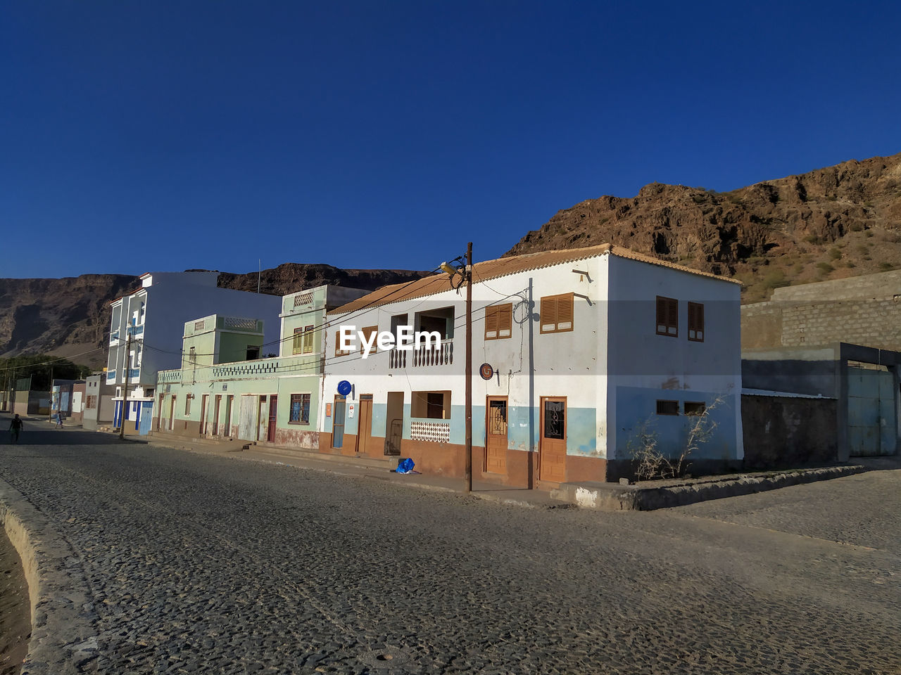 Road by buildings against clear blue sky