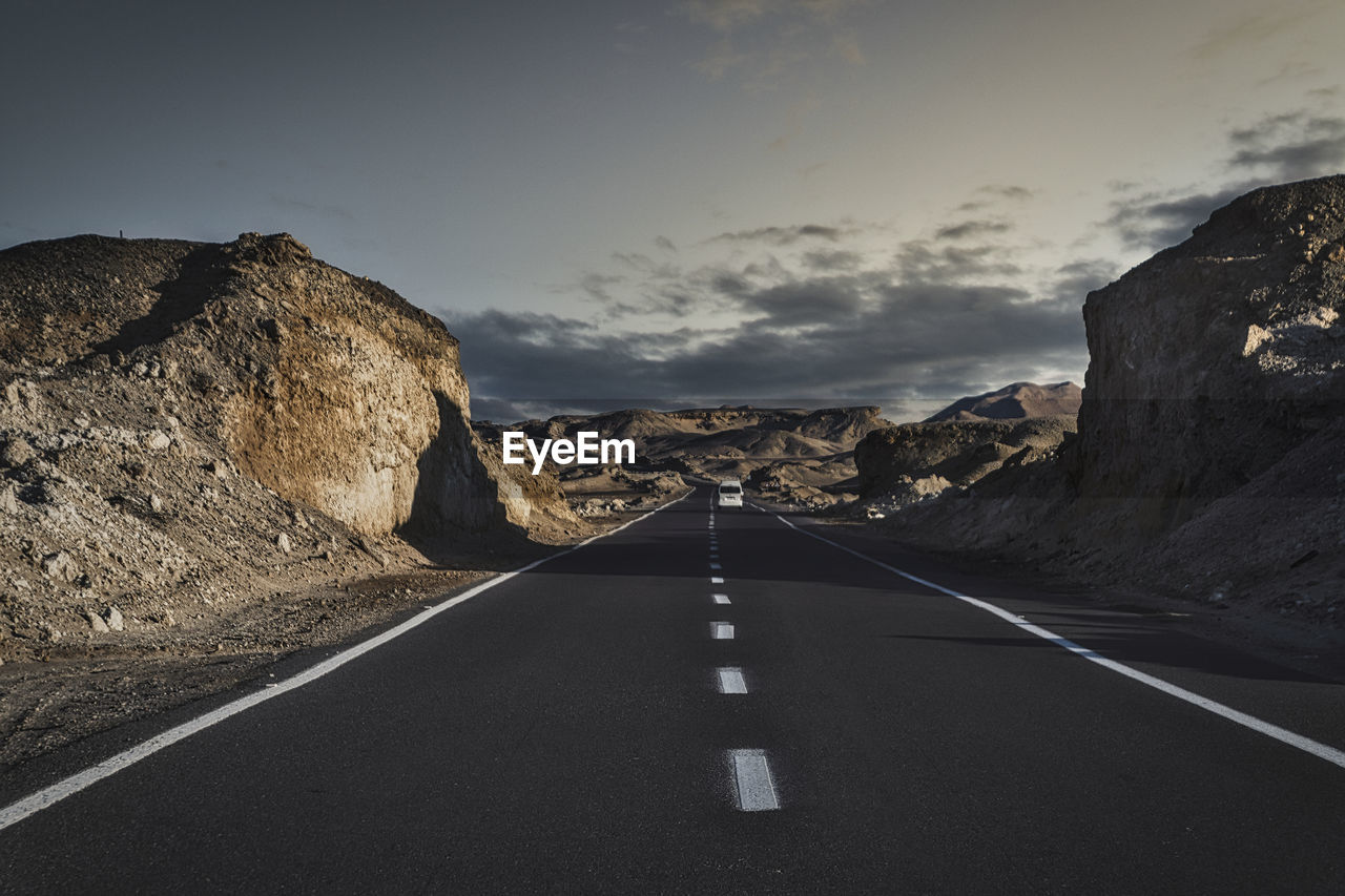 Empty road amidst desertmountains against sky