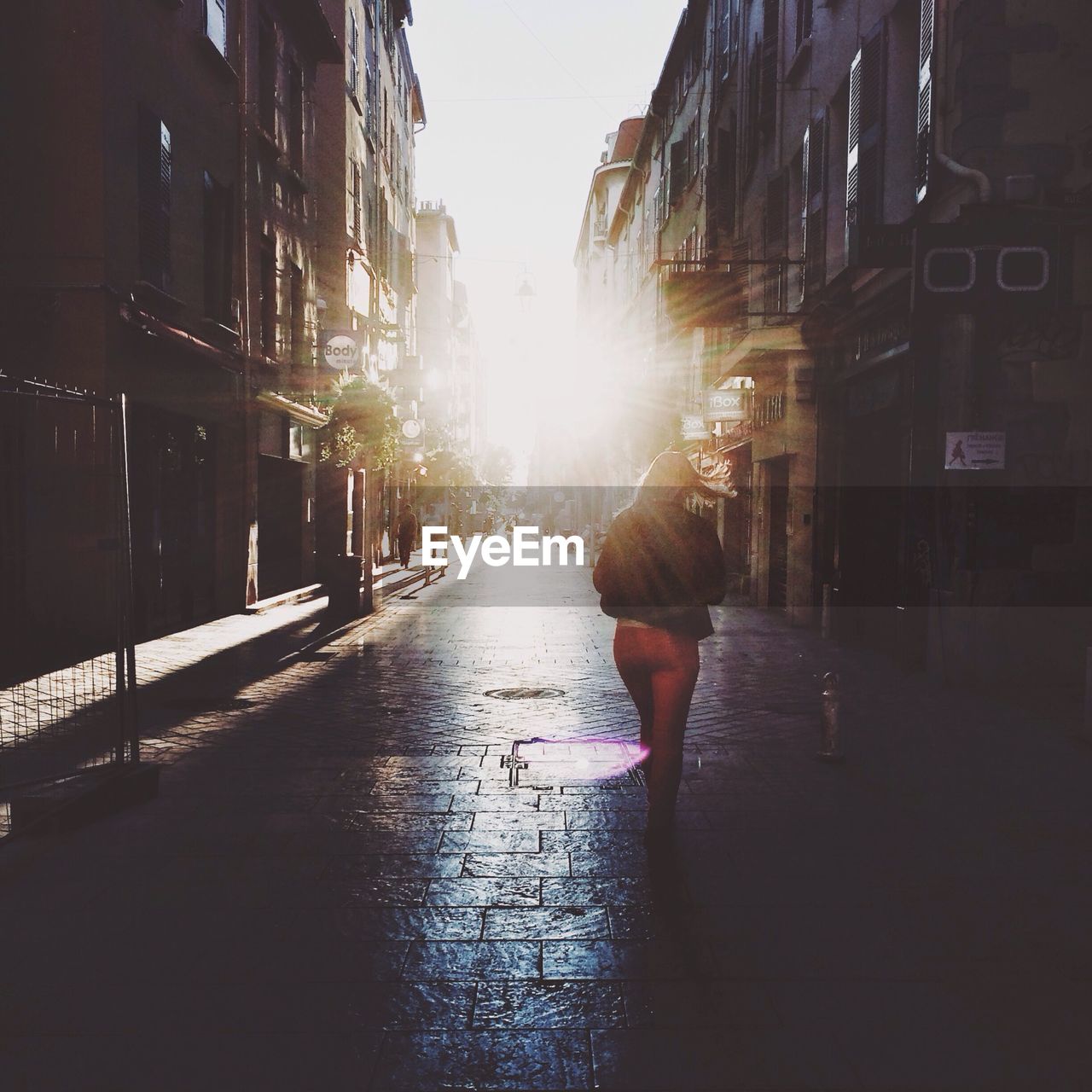 Rear view of woman walking on cobblestone street along buildings