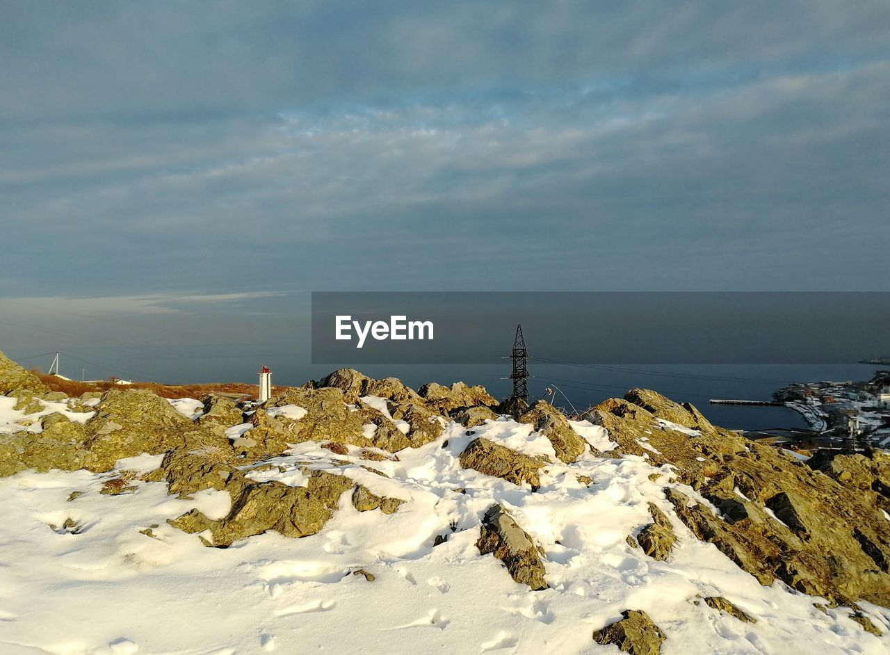 Snow covered rocks by sea against sky