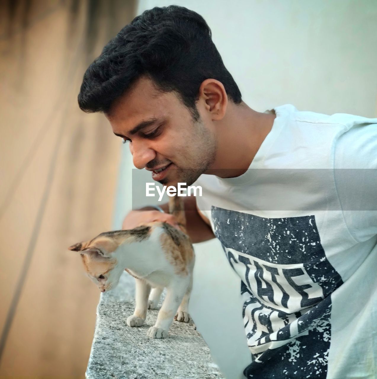 Close-up of young man looking down while holding kitten on retaining wall